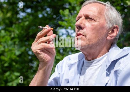 The senior enjoys a cigarette in the open air, a thought-provoking image on the themes of loneliness and parenting Stock Photo
