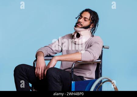 Arab man wearing cervical collar and sleeping while sitting in wheelchair. Young exhausted patient with closed eyes recovering from accident, using neck brace for spinal protection Stock Photo