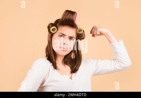 Woman with curlers. Funny housewife power. Pretty woman with curlers in her hair shows her strength and confidence. Stock Photo
