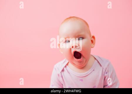 Portrait of a cute little yawning girl isolated on a pink background. A newborn baby yawns and wants to sleep Stock Photo