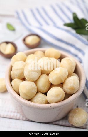 Tasty peeled Macadamia nuts in bowl on light table Stock Photo
