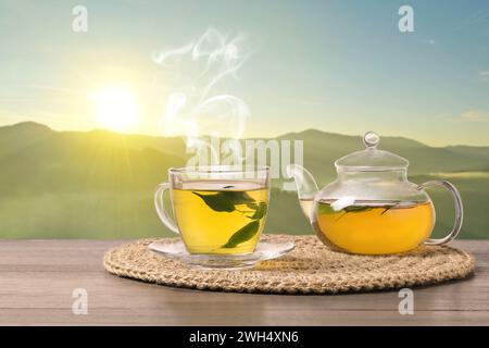 Aromatic green tea in glass cup and teapot on wooden table in mountains Stock Photo