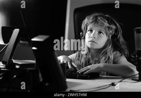 A little boy child uses a desktop at night, a child with computer screen in the room with neon lightning. School, study, online learning concept. Stock Photo