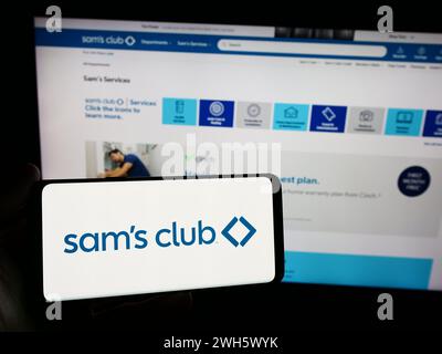 Person holding smartphone with logo of US membership-only retail stores company Sam's Club in front of website. Focus on phone display. Stock Photo