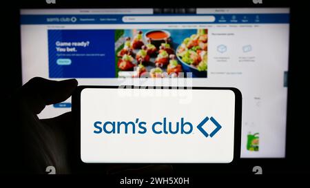 Person holding cellphone with logo of US membership-only retail stores company Sam's Club in front of business webpage. Focus on phone display. Stock Photo