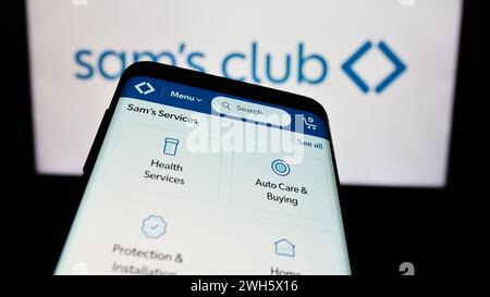 Mobile phone with website of US membership-only retail stores company Sam's Club in front of business logo. Focus on top-left of phone display. Stock Photo