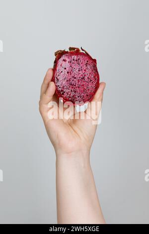 Pink Pitaya Dragon fruit in female hand on gray background. Cut red fleshed pitahaya fruit food closeup Stock Photo