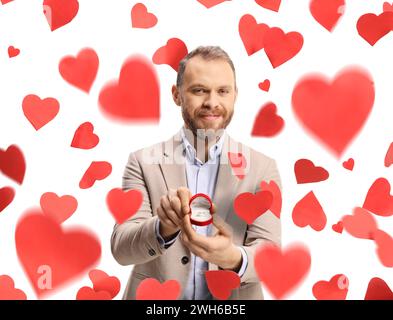 Man standing under falling hearts and holding an engagement ring in a box isolated on white background Stock Photo