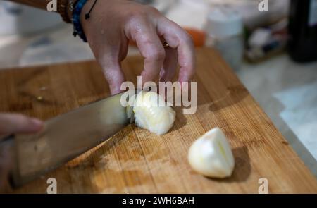 A person expertly dicing a fresh white onion on a rustic wooden cutting board Stock Photo