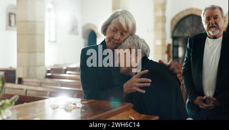 Senior women, coffin and funeral in church for memory, support and condolences with religion with family. Community, friends and together for death Stock Photo