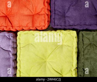 Top-down perspective of neatly arranged velour quilted cushions in bright orange, purple, yellow, and green. Handcrafted accessories for comfort and s Stock Photo