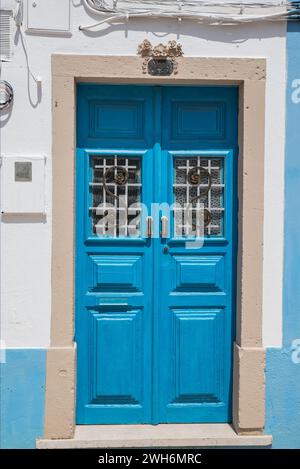 An old wooden blue double door with glass panels and scrollwork in Lagos, Portugal Stock Photo