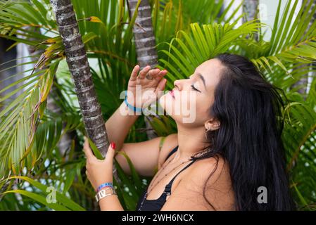 Portrait of beautiful young woman, with black hair, among leaves and branches of green plants posing for a photo. Person traveling. Stock Photo