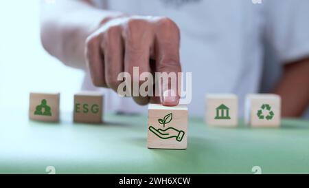 Man's hand touches a wooden cube with environmental and social governance symbols. ESG concept Stock Photo