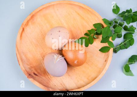 Whole chicken eggs in a wooden dish with green leaves on a white background Stock Photo