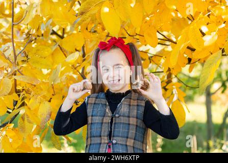 Smiling girl with red headband holds bowl of walnuts with autumn leaves in the background, capturing the essence of fall harvest and childhood joy. Au Stock Photo