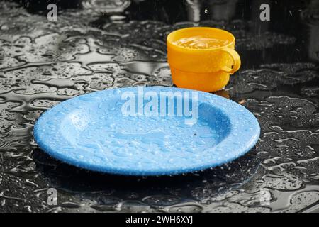 heavy rain falling on colourful childs cup and plate on an outdoor table in rain shower lake district cumbria england uk Stock Photo