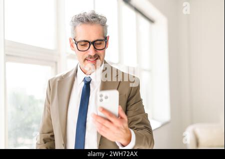 With a focused gaze, this seasoned businessman interacts with a smartphone, demonstrating the integration of cutting-edge technology into his wealth of professional experience. Mature man using phone Stock Photo