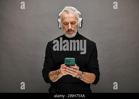 good looking mature male model with beard and headphones in black turtleneck looking at phone Stock Photo