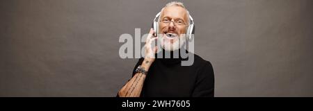 joyful handsome man in turtleneck with glasses and headphones smiling sincerely at camera, banner Stock Photo