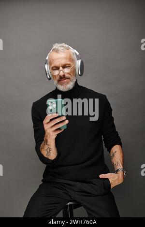 good looking mature male model with beard and headphones in black turtleneck looking at phone Stock Photo