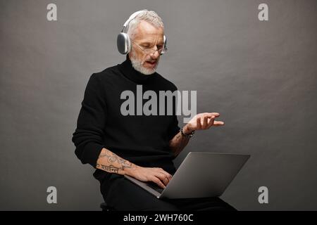 good looking bearded man in stylish black turtleneck with headphones sitting and having video call Stock Photo