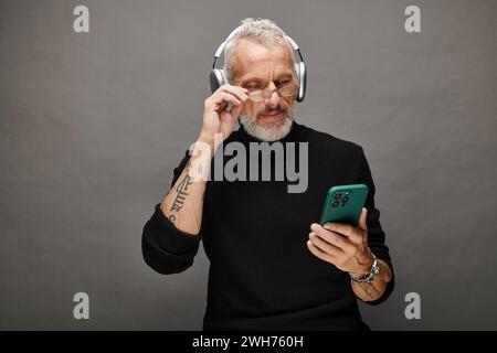 good looking mature male model with beard and headphones in black turtleneck looking at phone Stock Photo