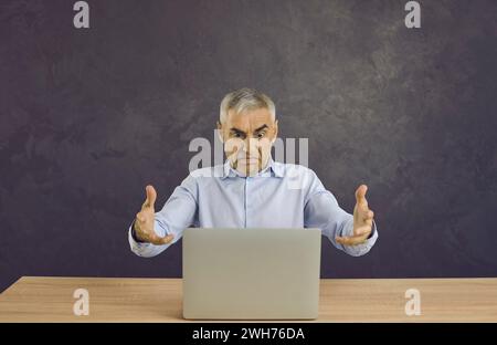 Outraged and angry man looking at screen reading bad news or having problems with broken laptop. Stock Photo