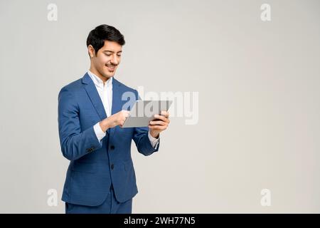 Young businessman in a business suit interacts with a digital tablet, his expression one of pleasant focus, perfect for illustrating the integration of modern technology in everyday professional tasks Stock Photo