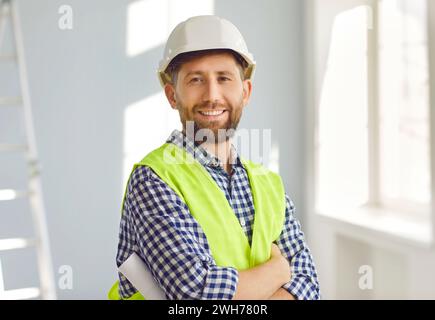 Portrait of positive, handsome young male construction worker in hard hat, smiling at the camera while working on construction site. Stock Photo