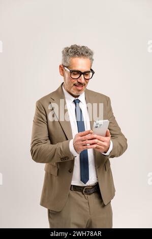 A senior businessman in formal suit and glasses is using a smartphone, representing the engagement with technology and connectivity of modern executives in the business world. Stock Photo