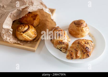 Fresh pastries - croissants with chocolate chips, poppy seed buns on a white sheet of paper on the table. Place for text Stock Photo