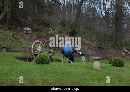 Friday Street Surrey England Man Sitting in Garden Looking towards Woodland and Wooden Wagon Wheel Made in to a Seat Stock Photo
