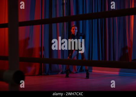 graceful dancer strikes a fierce pose in her black leotard and fishnet tights, framed by curtain Stock Photo