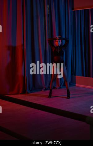 woman in fishnet tights and high heels strikes a graceful pose near curtain during performance Stock Photo