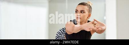 A graceful dancer in zebra shorts and black top stretches body against wall in studio, banner Stock Photo