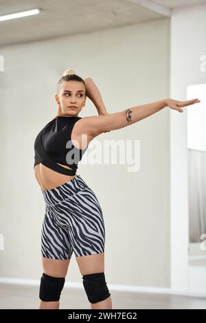 A graceful dancer stretches her body and arms in vibrant zebra shorts and a black top, flexibility Stock Photo