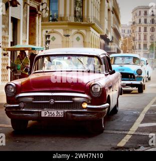 Red and blue vintage classic Cuban American cars driving through an Havana city street, past classic old city architecture Stock Photo