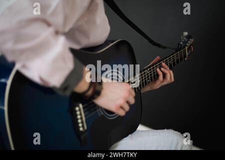 A young slim attractive man in white shirt playing  blue guitar on black  background, close up Stock Photo