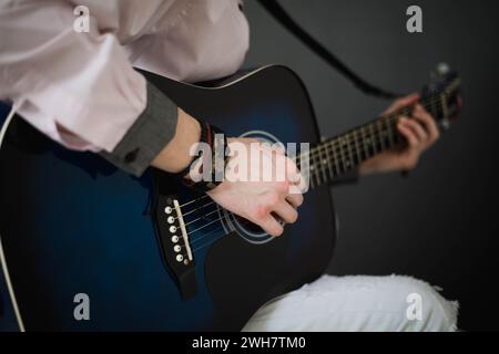 A young slim attractive man in white shirt playing  blue guitar on black  background, close up Stock Photo