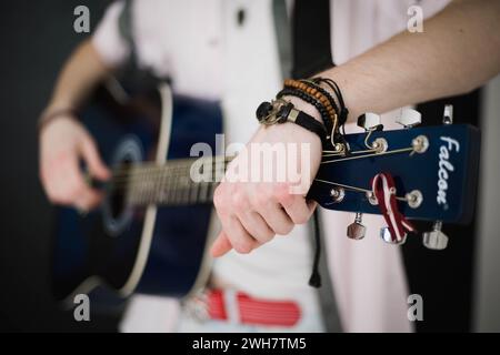 A young slim attractive man in white shirt playing  blue guitar on black  background, close up Stock Photo