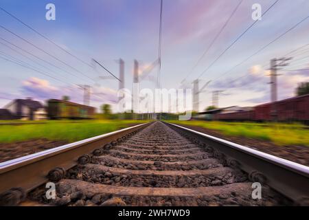 Railroad in motion with motion blur effect at sunset with beautiful sky and purple clouds. Railway transportation. Stock Photo