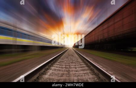 Railroad in motion at sunset with dramatic sky. Motion blur effect. Train traveling on the railway. Stock Photo