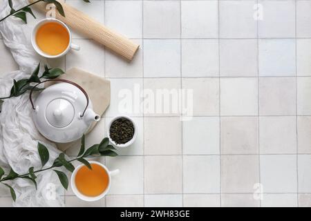 Composition with teapot, cups of tea and bowl with dry leaves on white tile background Stock Photo