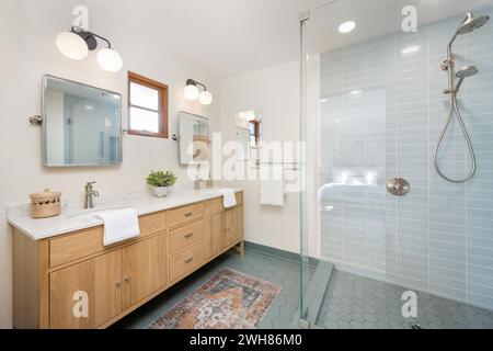 White bathroom with tiled walls, wooden cabinets, and sky blue tiled floor Stock Photo