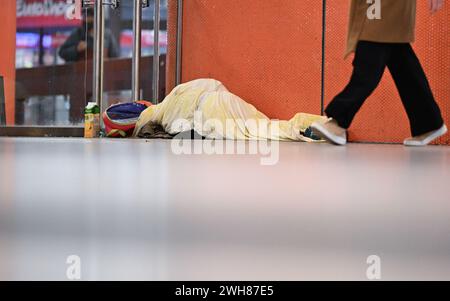 Stuttgart, Germany. 08th Feb, 2024. A passer-by walks past a person lying on the ground in the Klett Passage at Stuttgart Central Station. Credit: Bernd Weißbrod/dpa/Alamy Live News Stock Photo