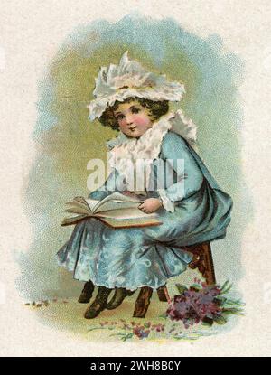 A charming Victorian colour print of a young girl sitting on a stool, reading a book. She is wearing a blue dress with a lace collar and bonnet. Stock Photo