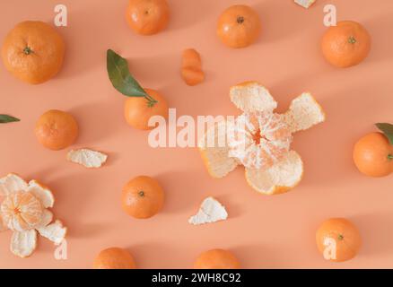 Trendy fruit pattern made of many fresh ripe tangerines and green leaves on light peachy orange background. Minimal citrus fruit concept. Stock Photo