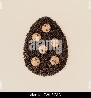 Creative composition with Easter egg shape made of roasted coffee beans and chocolate cookies on light cream background. Trendy Easter egg idea. Stock Photo