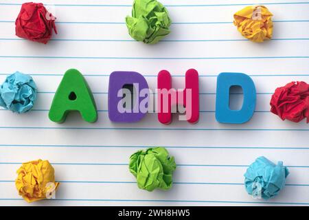 ADHD. The abbreviation ADHD on a notebook sheet with some colorful crumpled paper balls around it. Close up. ADHD stands for Attention deficit hyperac Stock Photo